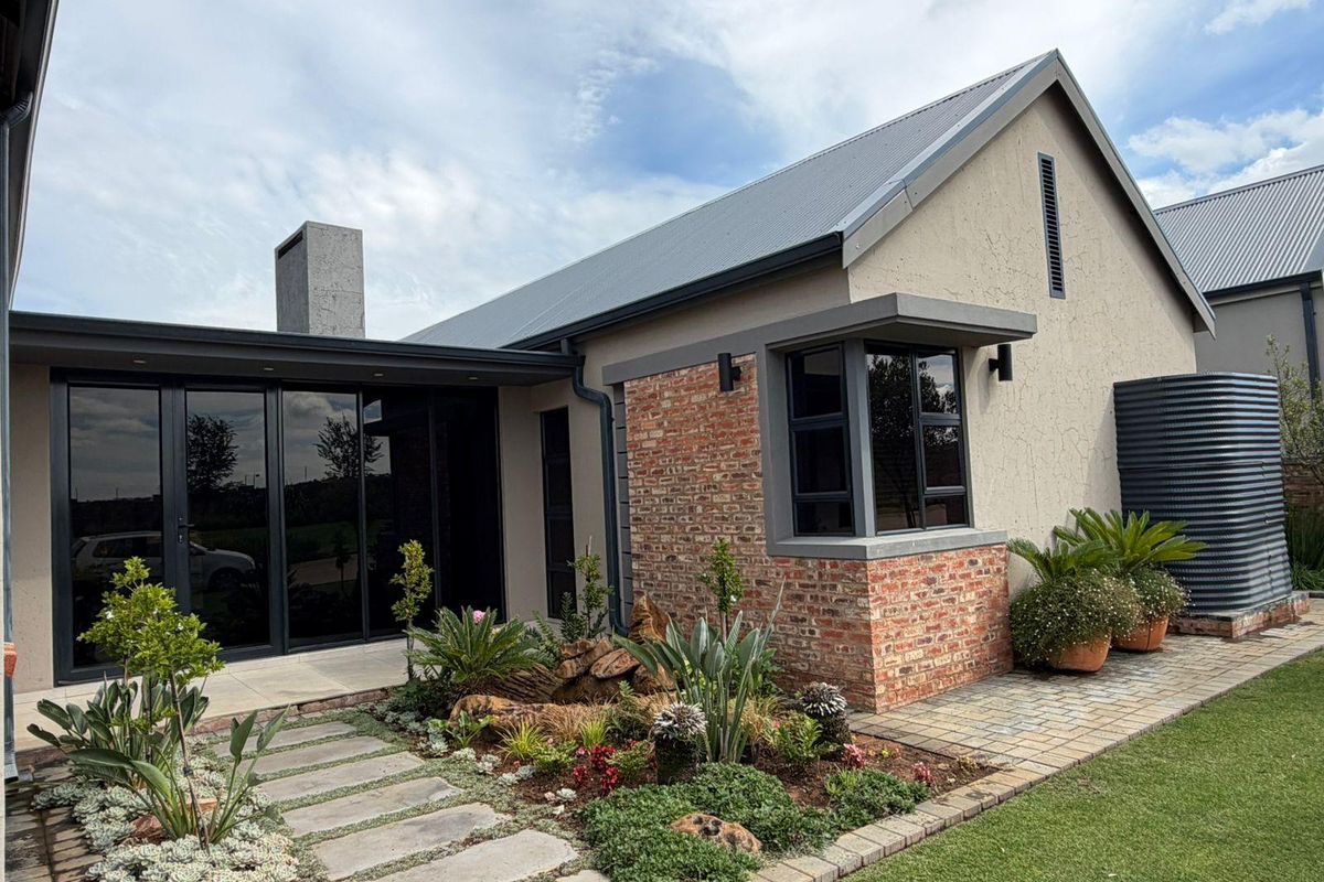 A well-maintained rear exterior view featuring a modern blend of brick and plaster finishes, aluminium glazing, and a landscaped garden with a paved walkway.