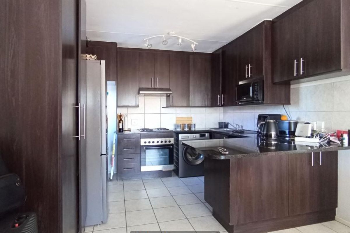 A functional kitchen featuring dark wood cabinetry, granite countertops, built-in oven, hob, and integrated laundry appliances with tiled flooring and backsplash.