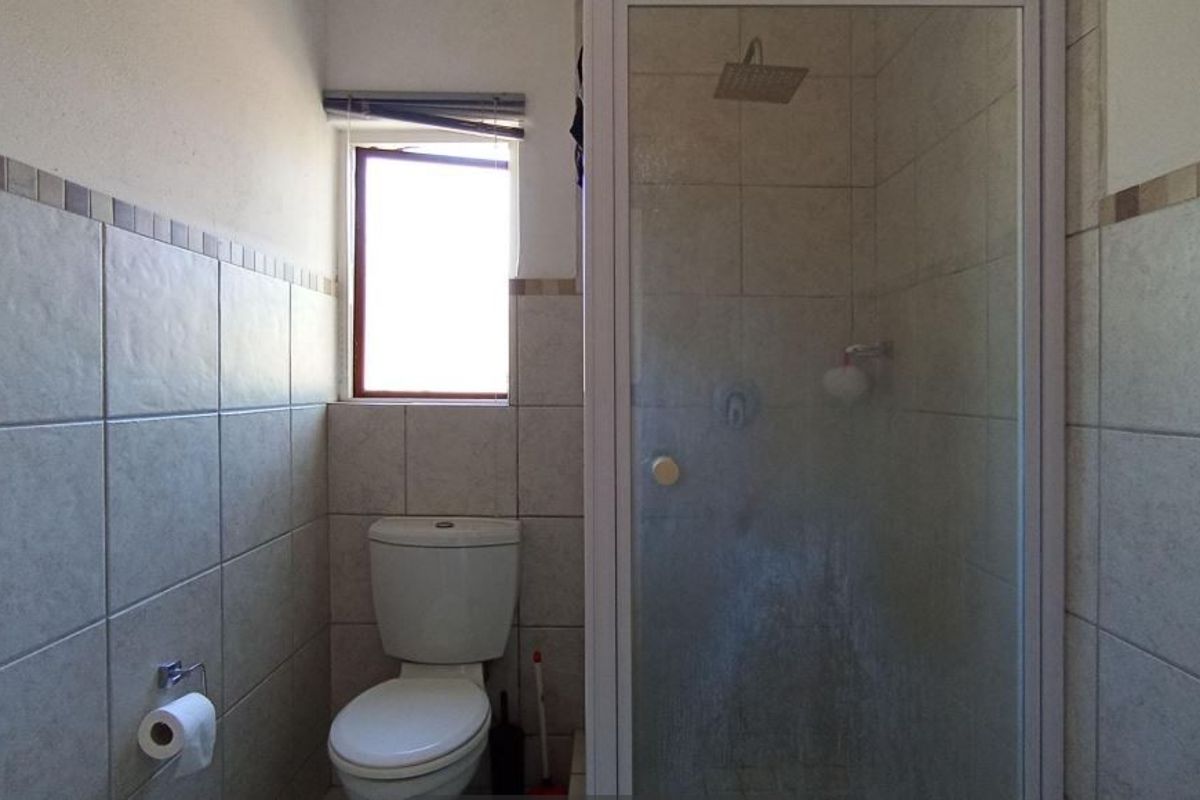 A functional bathroom featuring a tiled shower enclosure, a standard toilet, and a window, providing a clean and practical space.