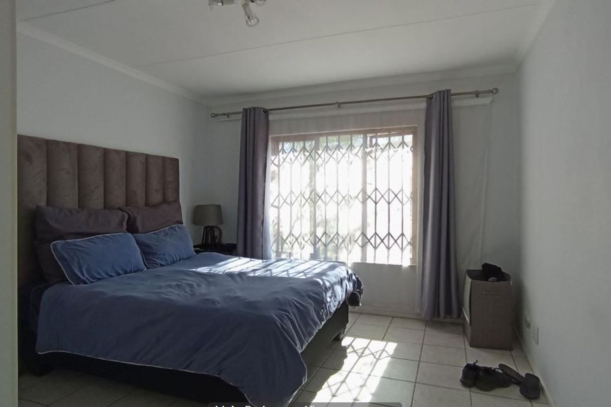 A functional bedroom featuring tiled flooring and a window fitted with a security gate, providing natural light and essential security.