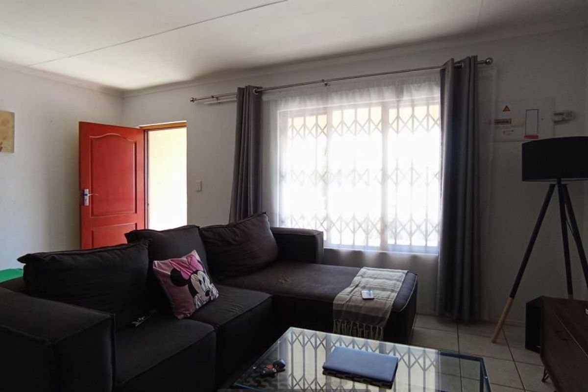 A living room featuring tiled flooring, a security gate on the window, and a wall-mounted electrical distribution board.