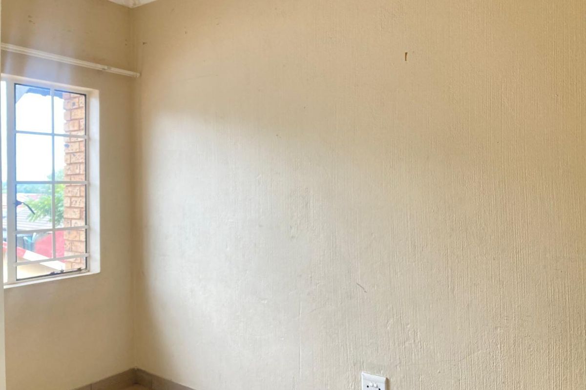 An empty bedroom featuring textured walls, a window with security bars, and a standard electrical outlet.