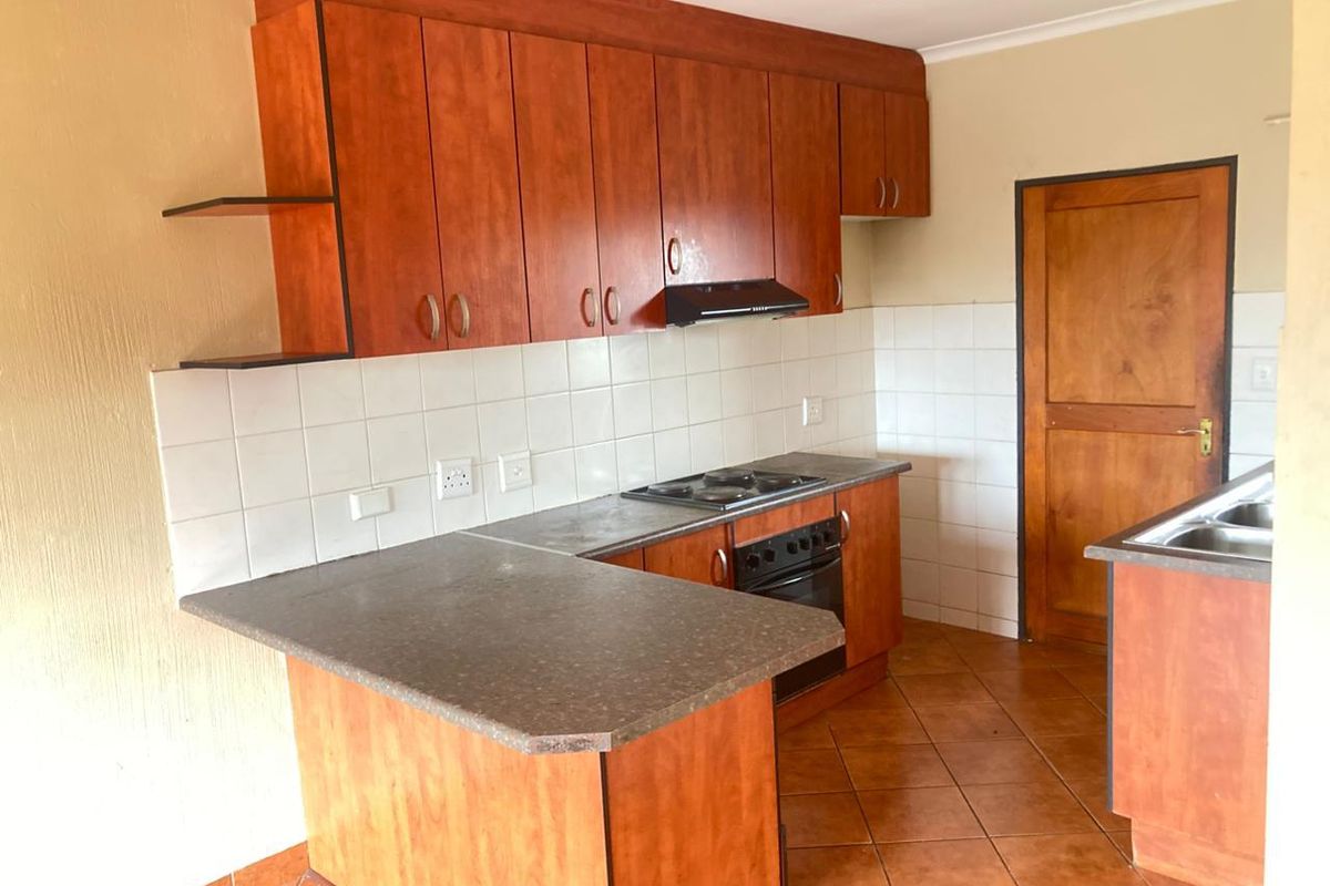 A functional kitchen featuring wooden cabinetry, built-in oven and hob, tiled splashbacks, and a double sink, offering a practical layout for daily use.
