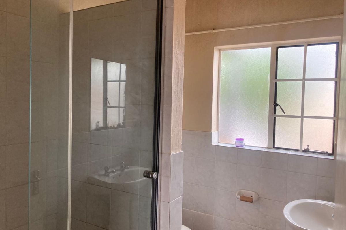 A functional bathroom featuring a glass shower enclosure, pedestal basin, and tiled walls, requiring cosmetic updates to improve its overall condition.