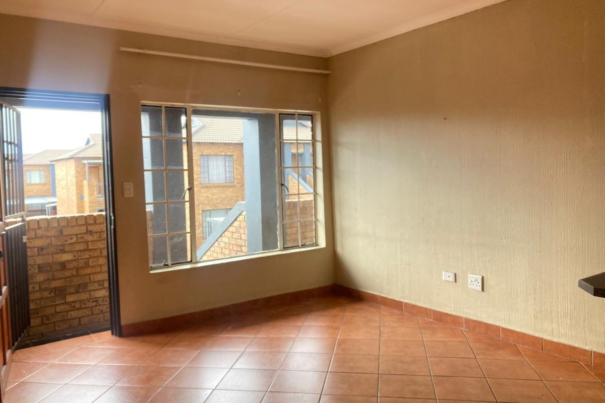 An empty living area featuring tiled flooring, security gate access, and large windows with security bars, offering a blank canvas for interior design.