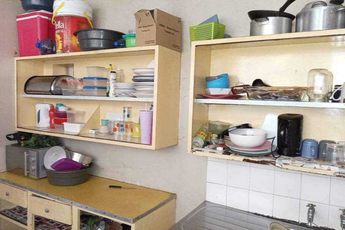 A dated kitchen area featuring built-in cabinetry, a stainless steel sink, and tiled splashback, currently showing signs of wear and tear.
