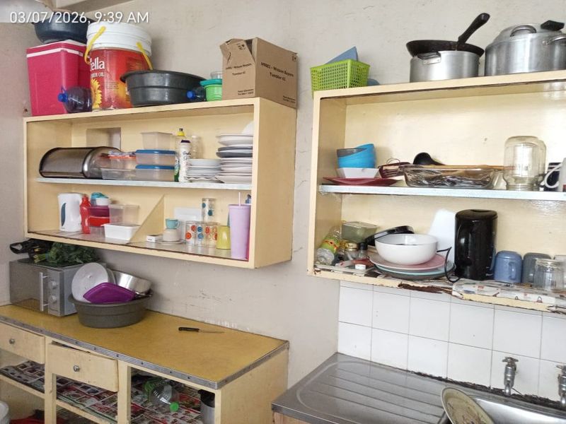 A dated kitchen area featuring built-in cabinetry, a stainless steel sink, and tiled splashback, currently showing signs of wear and tear.