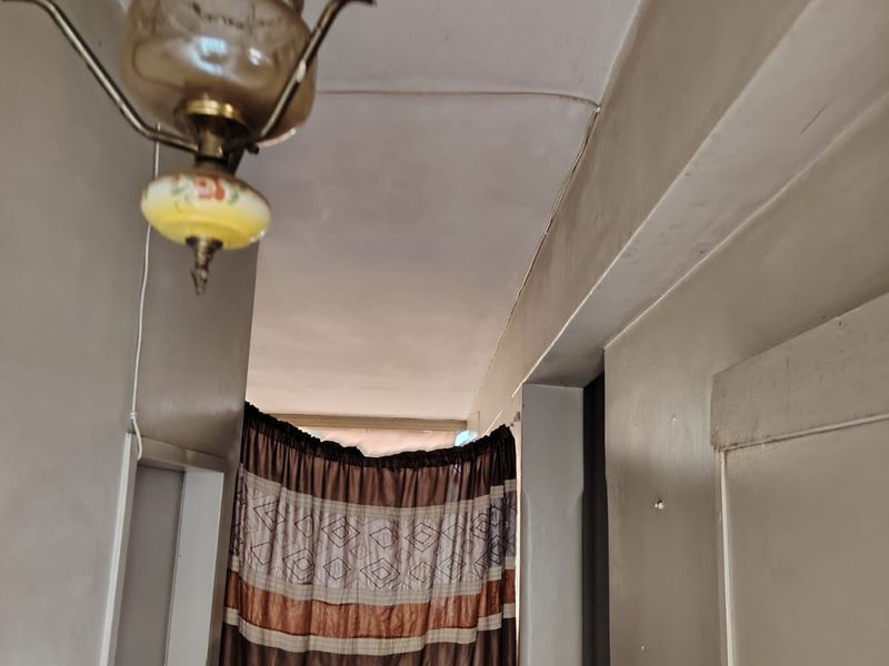 A narrow hallway featuring a vintage pendant light fixture and painted walls with visible signs of wear and ceiling cracks.