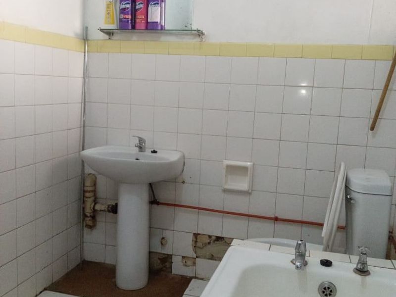 A dated bathroom featuring a pedestal basin, bathtub, and toilet, with visible wall tile damage and exposed plumbing requiring maintenance or renovation.