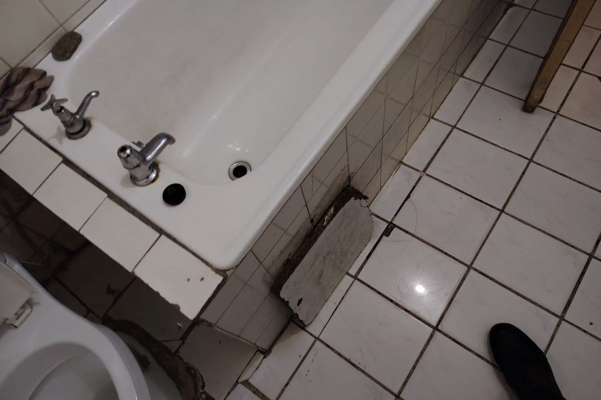 A bathroom featuring a bathtub and tiled flooring, currently showing significant wear and damage to the bath surround and tiling.