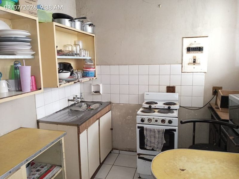 A dated kitchen featuring basic cabinetry, a stainless steel sink, and a freestanding stove, requiring significant cosmetic updates and repairs to wall finishes.