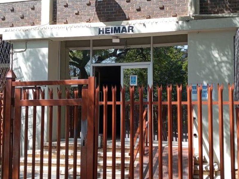Front entrance of the Heimar apartment building featuring a brick facade, secure metal gate, and accessible ramp entry.