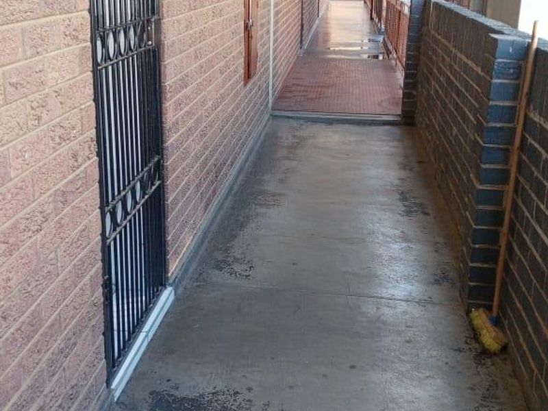 An exterior apartment hallway featuring brick walls, security gates, and concrete flooring showing signs of wear.