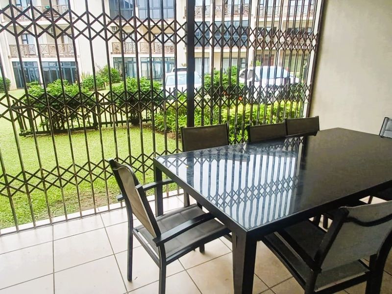 A covered patio area featuring tiled flooring and secure metal security gates, overlooking a communal garden space.