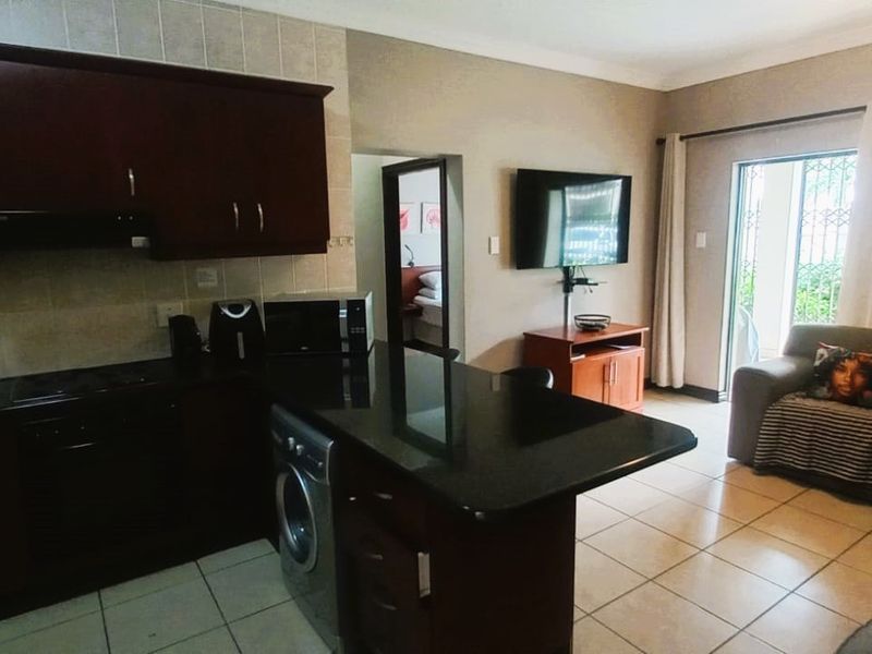 Open-plan living area featuring a kitchen with dark cabinetry, granite countertops, and tiled flooring, seamlessly flowing into the adjacent lounge space.