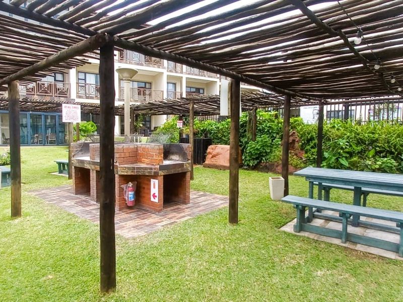 Communal outdoor entertainment area featuring a covered pergola, built-in brick braai facility, and landscaped garden space.