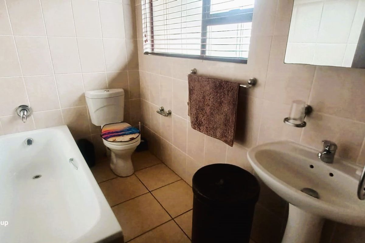 A functional bathroom featuring a bathtub, pedestal basin, and toilet with tiled walls and flooring.