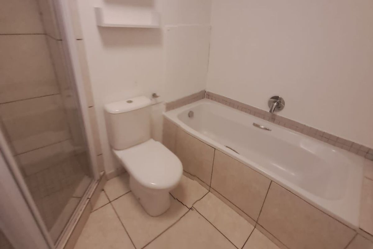 A functional bathroom featuring a separate shower enclosure, a bathtub with tiled surround, and a toilet, with some visible wear to the floor tiles.