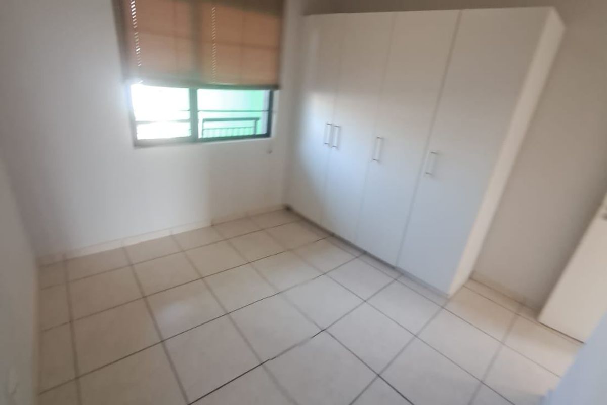 A clean, empty bedroom featuring neutral tiled flooring and a built-in white wardrobe, providing a blank canvas for personalization.