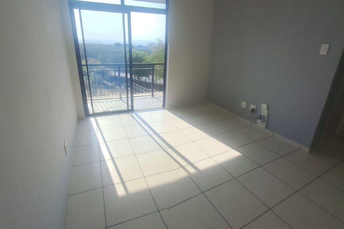 An empty living area featuring neutral tiled flooring, a grey accent wall, and a sliding glass door providing access to a balcony.