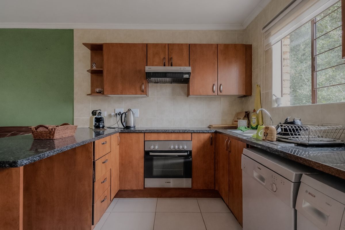 A functional U-shaped kitchen featuring wooden cabinetry, granite countertops, a built-in oven, and a tiled backsplash with a window for natural light.
