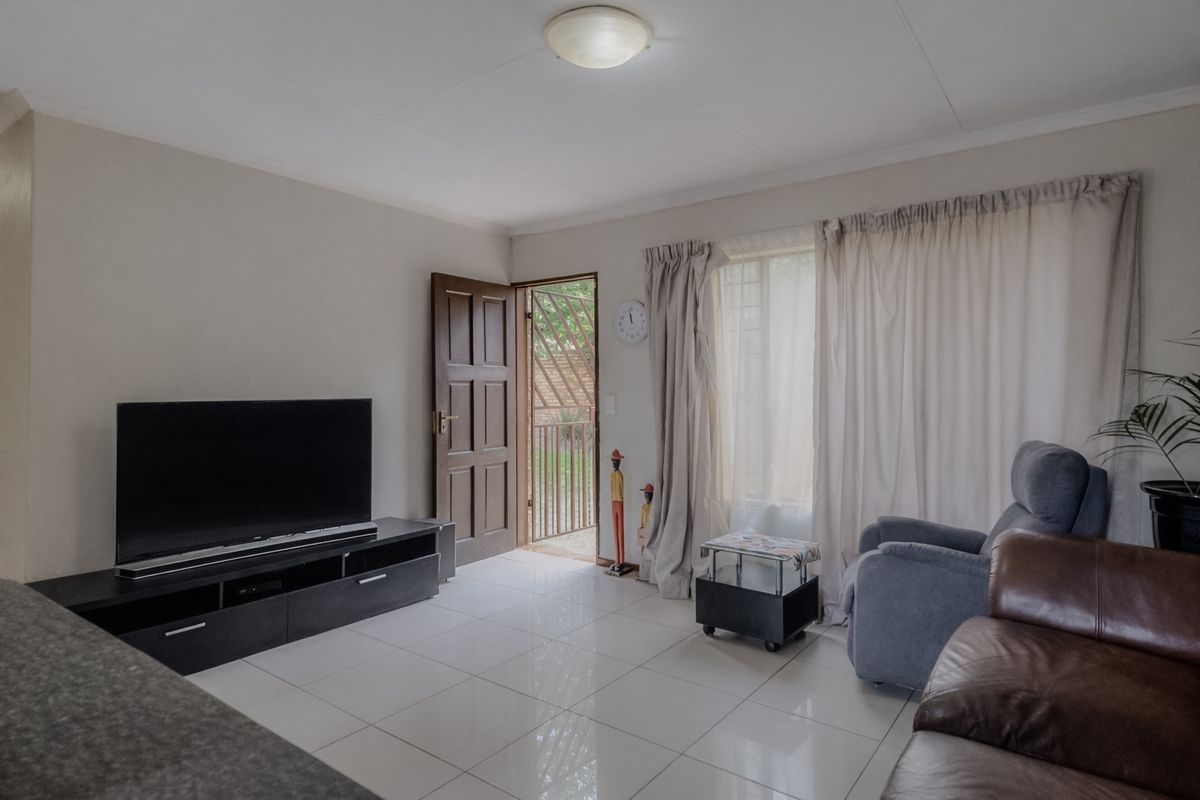 A living room featuring neutral tiled flooring, a flush mount ceiling light, and direct access to an outdoor area through a timber door.