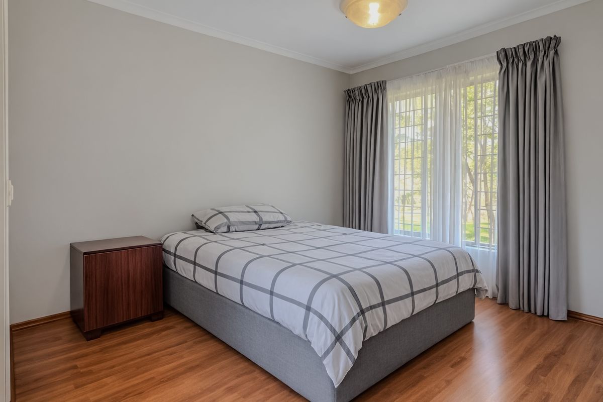 A well-maintained bedroom featuring laminate flooring, neutral wall tones, and a large window with natural light.