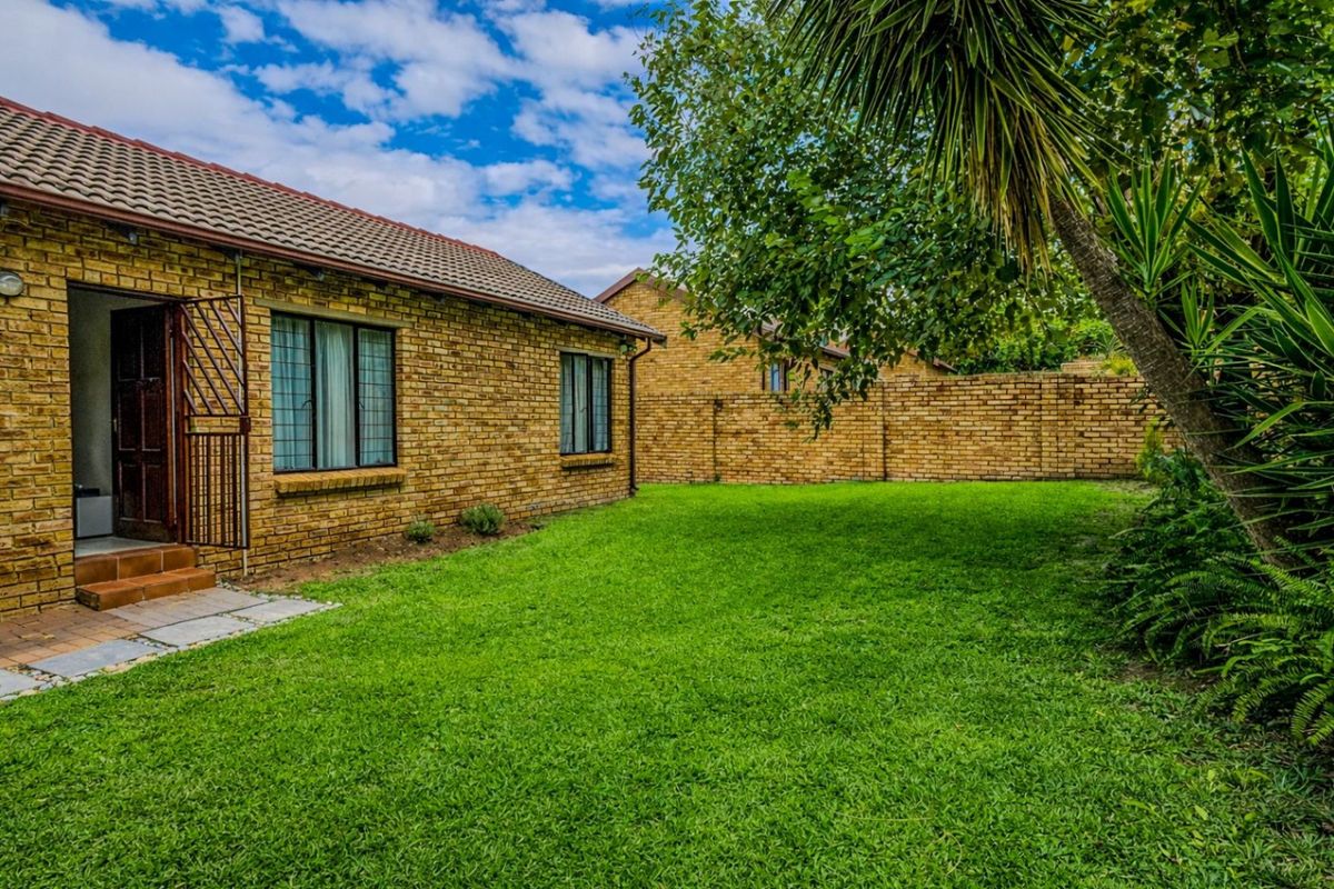 A well-maintained rear exterior view of a face brick townhouse featuring a private garden, paved walkway, and secure access door.