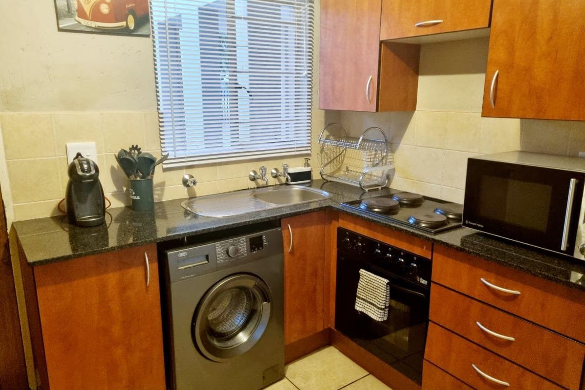 A functional kitchen featuring granite countertops, wood-finish cabinetry, a built-in oven with electric hob, and a stainless steel sink.