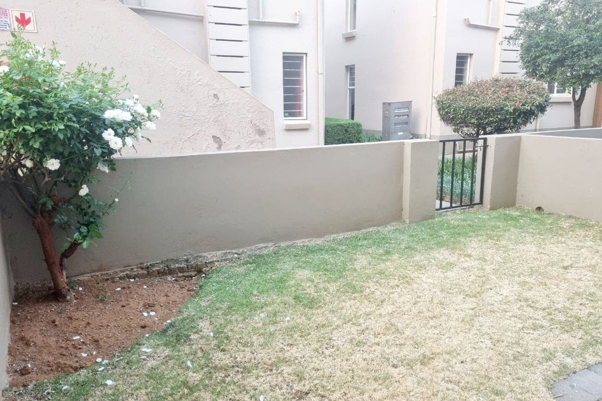 A private rear garden area featuring a lawn, paved section, and a boundary wall with a small pedestrian gate.