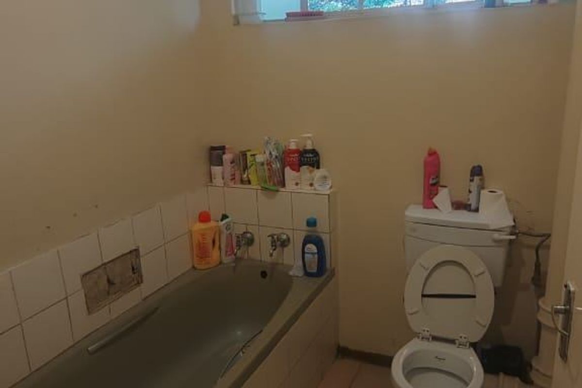 A dated bathroom featuring a built-in bathtub, a standard toilet, and tiled flooring, requiring cosmetic updates to modernize the space.