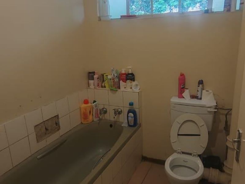 A dated bathroom featuring a built-in bathtub, a standard toilet, and tiled flooring, requiring cosmetic updates to modernize the space.
