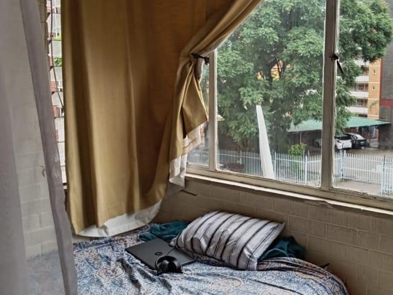 A compact enclosed balcony area featuring large windows with exterior views, tiled flooring, and wood-paneled ceiling detail.