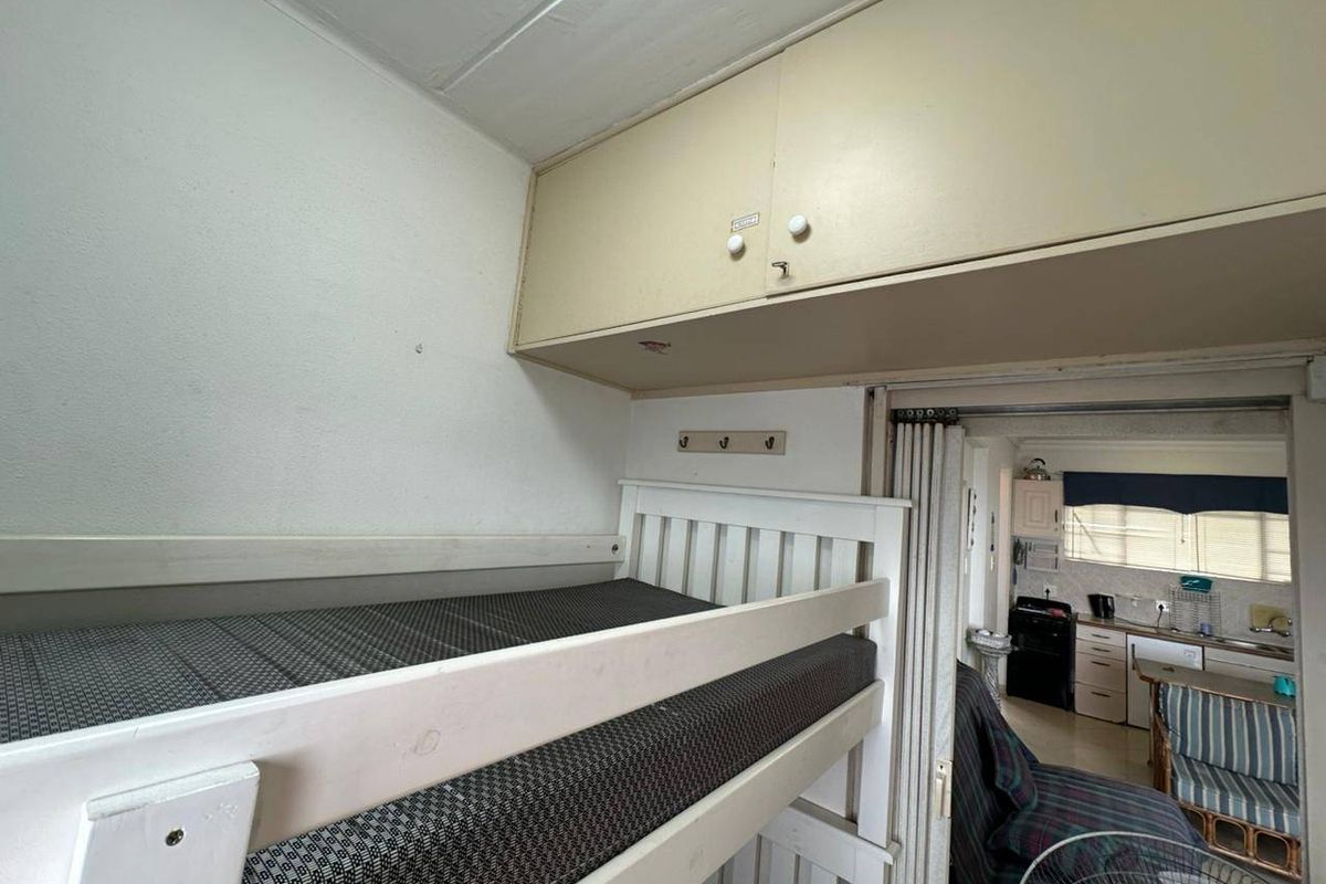 Compact bedroom featuring built-in overhead storage cabinetry and a folding partition door, providing direct access to the adjacent kitchen area.