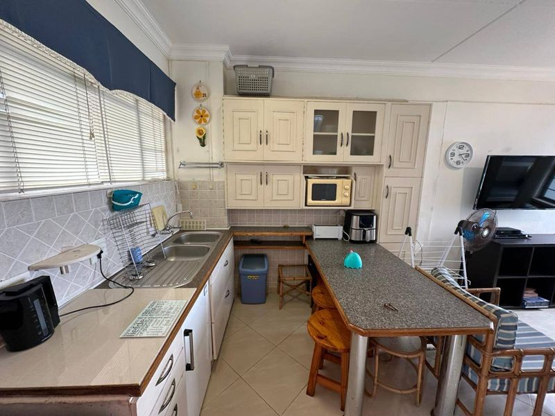Open plan kitchen area featuring built-in cabinetry, double sink, tiled backsplash, and integrated microwave, seamlessly flowing into the living space.