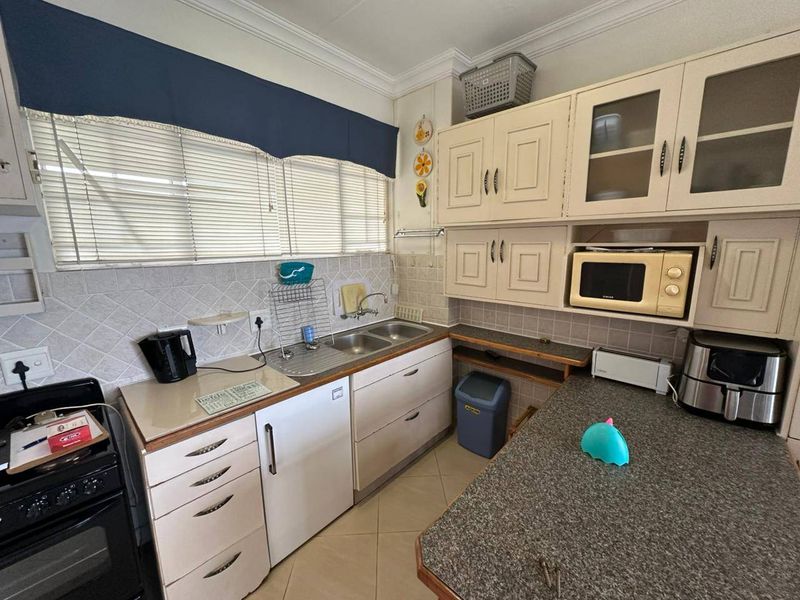 A functional kitchen featuring built-in cabinetry, a double basin sink, tiled backsplash, and laminate countertops, offering a practical layout for daily use.