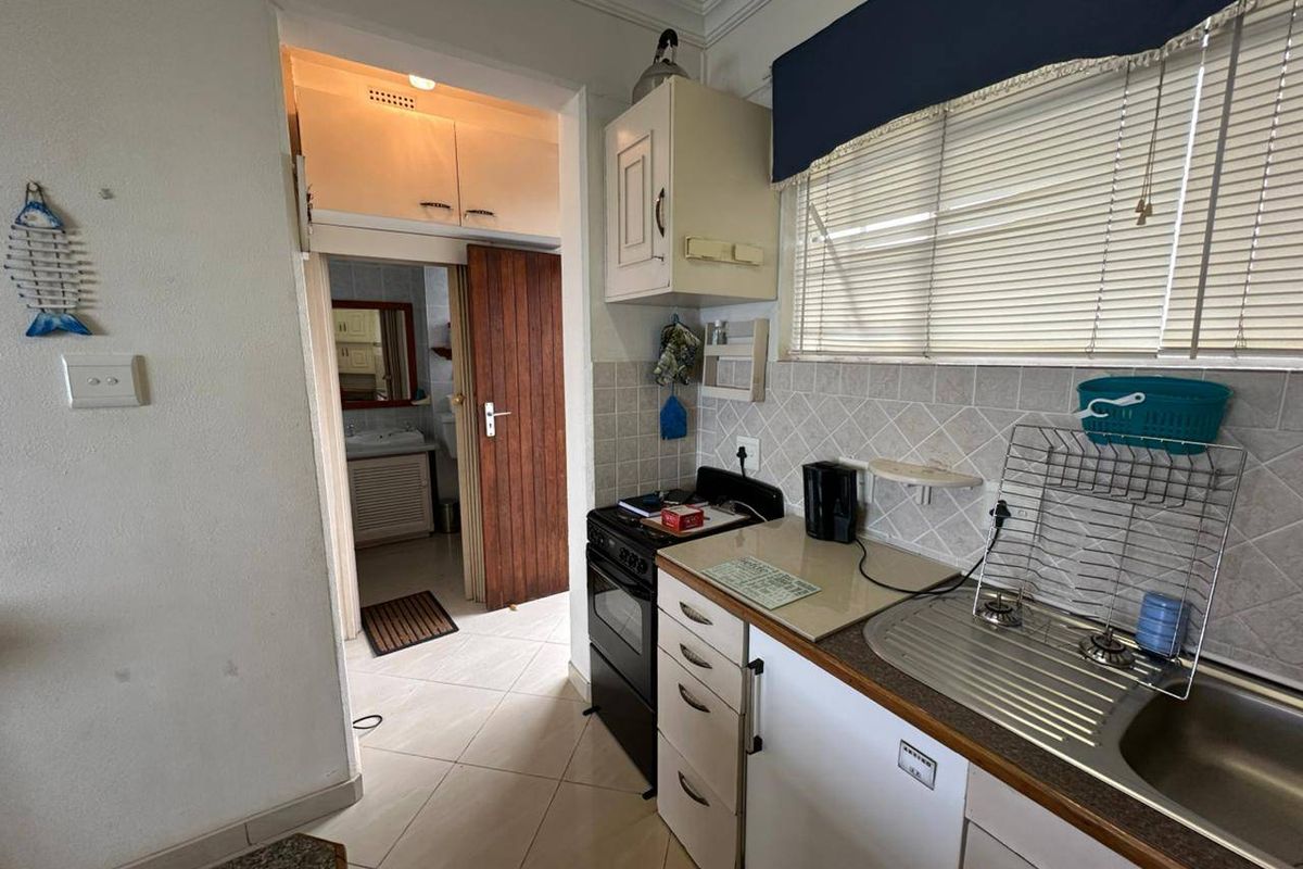 A functional kitchen featuring tiled backsplash, built-in cabinetry, and a stainless steel sink, with direct access to an adjacent bathroom area.