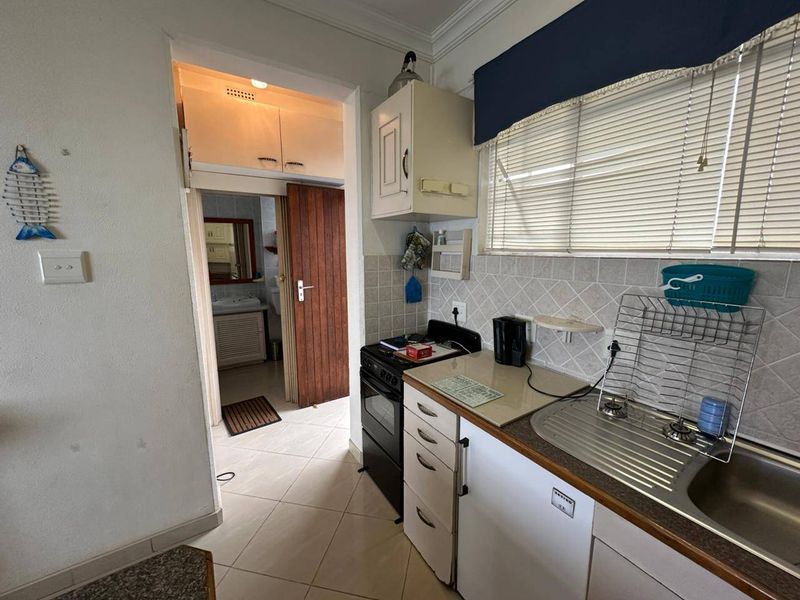 A functional kitchen featuring tiled backsplash, built-in cabinetry, and a stainless steel sink, with direct access to an adjacent bathroom area.