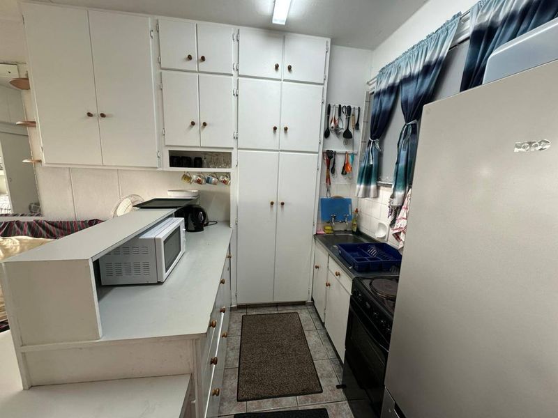 A compact kitchen featuring white built-in cabinetry, laminate countertops, and an electric stove, offering a functional layout with potential for modernization.