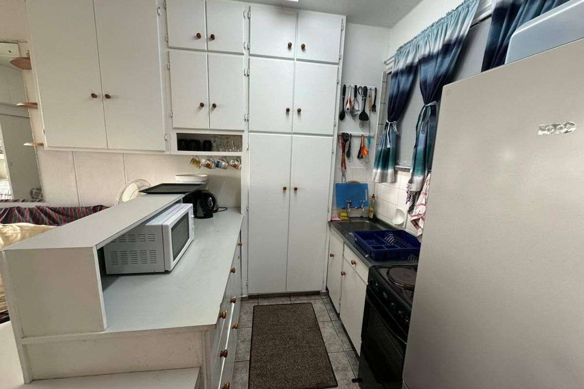 A compact kitchen featuring white built-in cabinetry, laminate countertops, and an electric stove, offering a functional layout with potential for modernization.