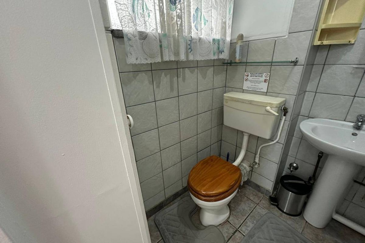 A compact bathroom featuring a pedestal basin and standard ceramic toilet with tiled walls and flooring.
