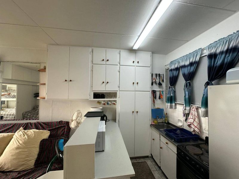 Compact kitchen featuring white built-in cabinetry, a breakfast bar, and an integrated electric stove, offering a functional layout in need of cosmetic updates.