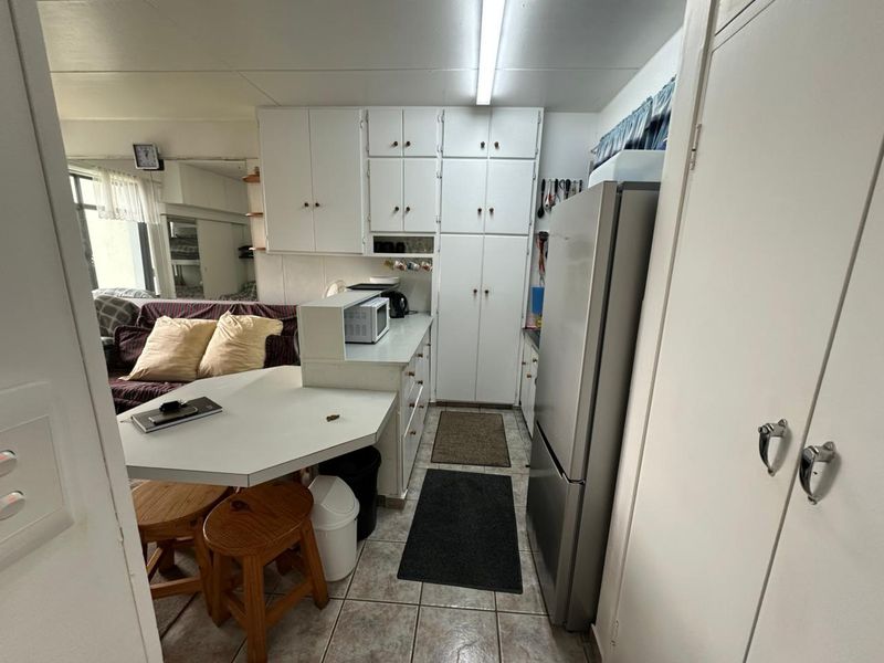 Compact open-plan kitchen area featuring white built-in cabinetry, a breakfast bar, and tiled flooring, integrated with the adjacent living space.