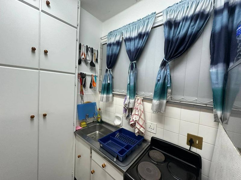 Compact kitchen featuring built-in cabinetry, a stainless steel sink, tiled backsplash, and an electric hob, offering a functional layout for a small apartment.