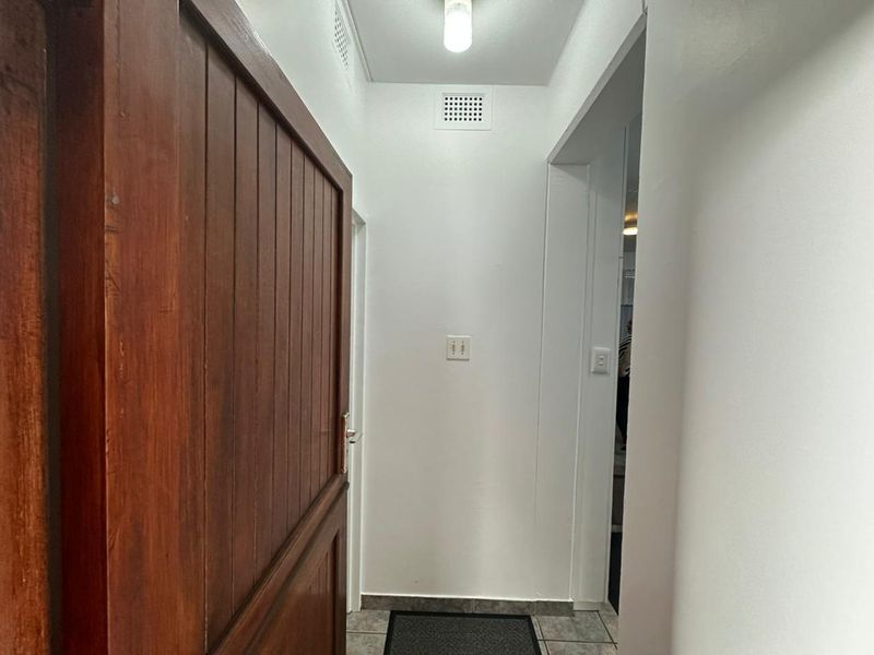 A functional hallway featuring tiled flooring and a solid timber door, providing access to adjacent living areas.