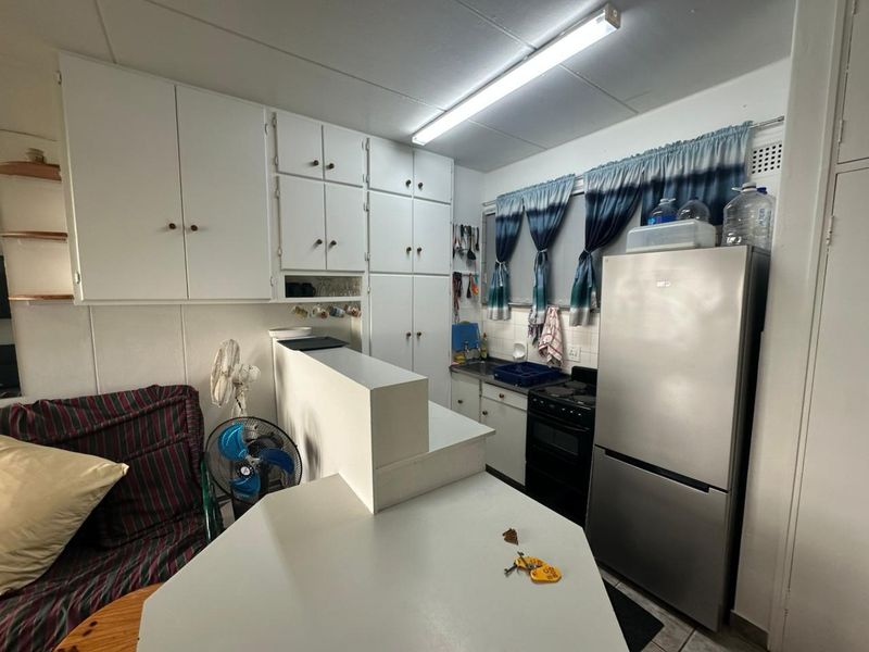 Compact kitchen featuring white built-in cabinetry, a tiled splashback, and a functional layout with a breakfast bar counter.