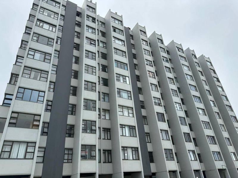 A low-angle view of a modern multi-story apartment building facade featuring uniform concrete construction and large aluminum-framed windows.