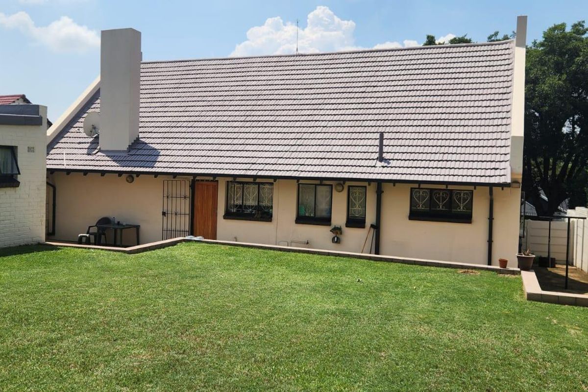 Rear view of the property featuring a tiled roof, chimney, and a built-in outdoor braai area set within a private garden.