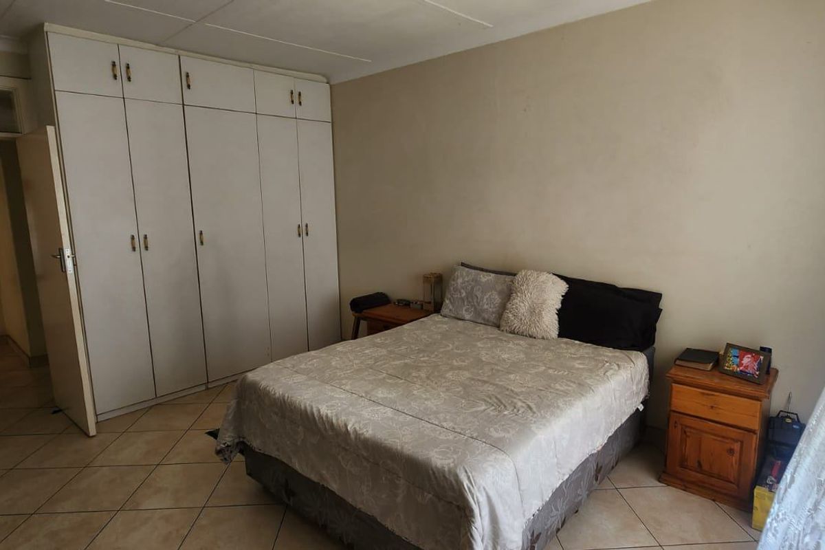 A bedroom featuring built-in cupboards, tiled flooring, and neutral wall finishes, offering a functional space with potential for cosmetic updates.