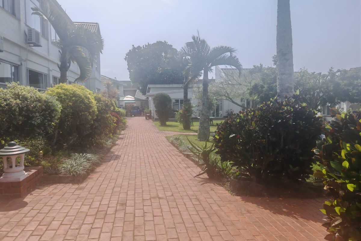 A well-maintained brick paved pathway leading through a landscaped garden area between apartment building wings.